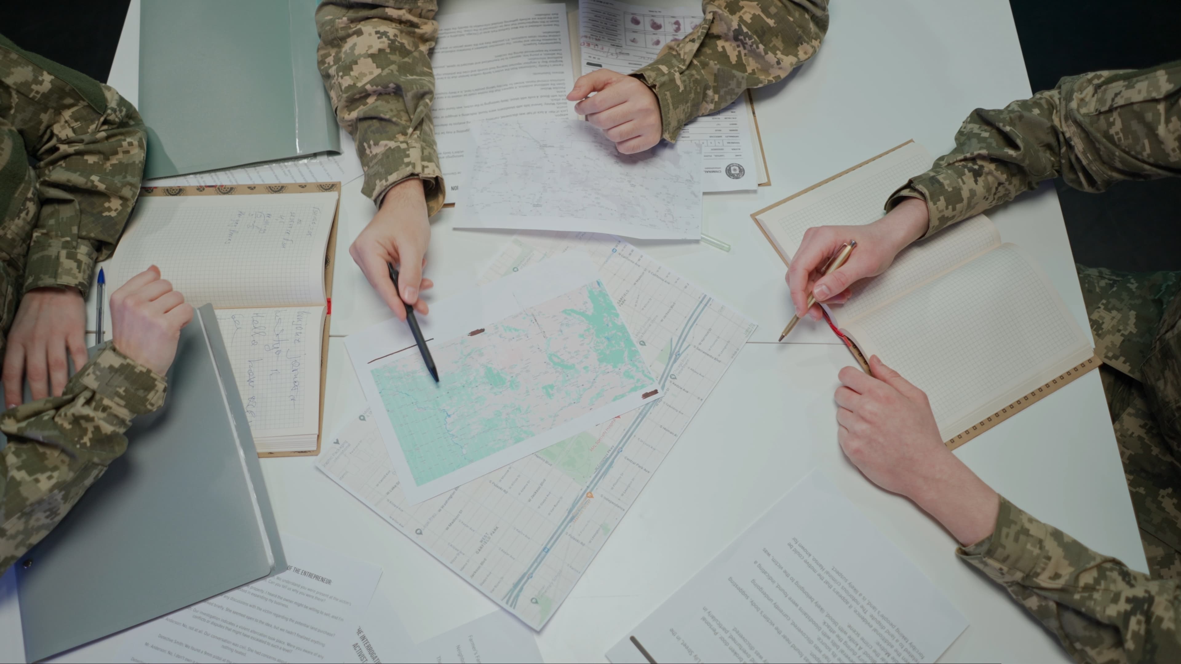 Military team around a planning table with maps, notebooks and documents.